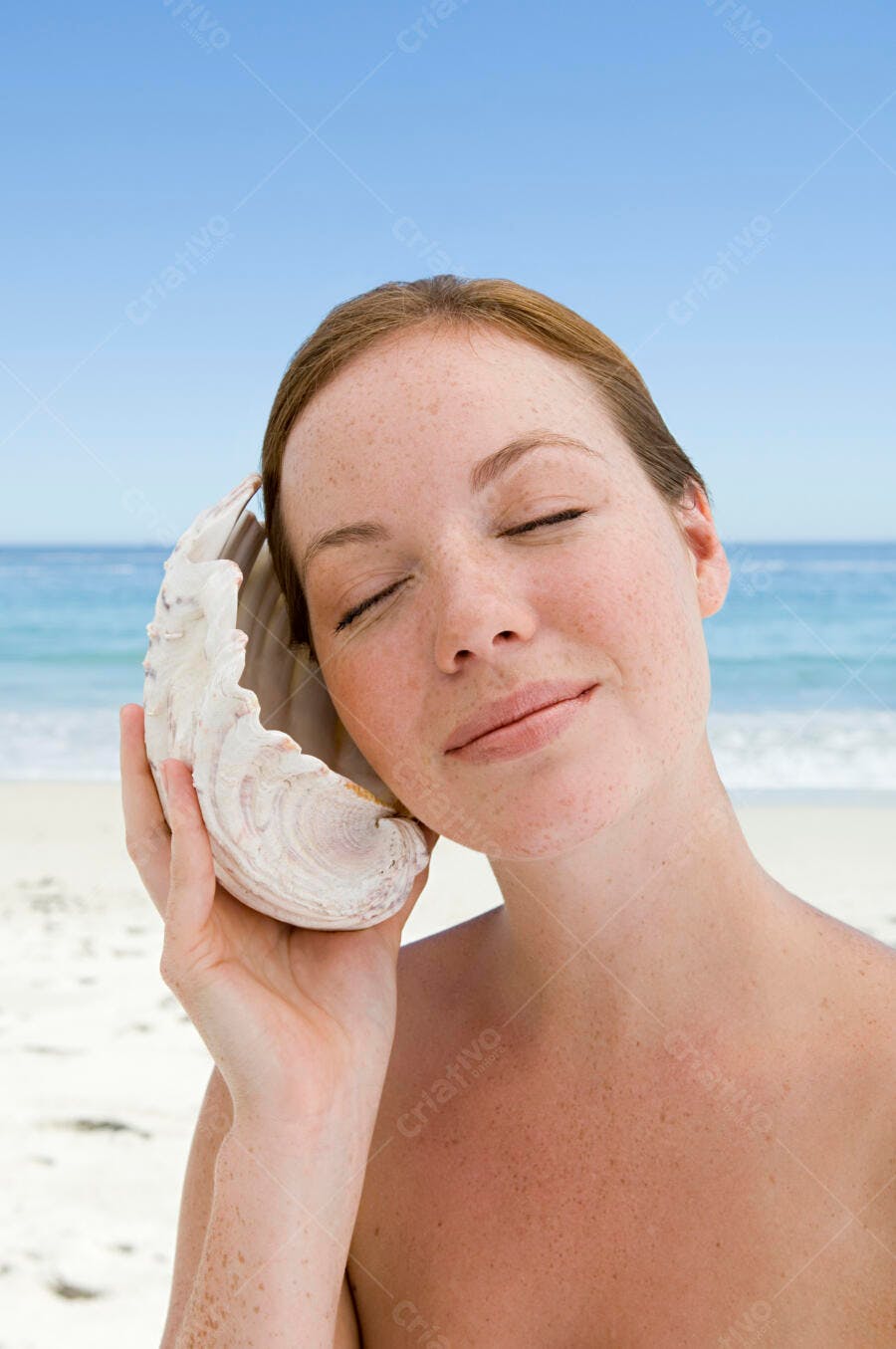 Mulher na praia ouvindo concha do mar