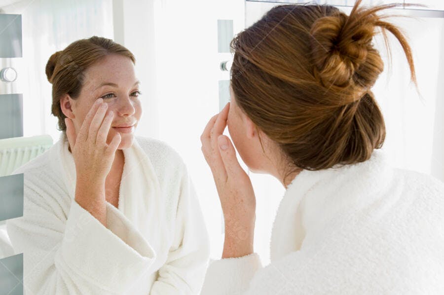 Mulher aplicando creme facial no espelho