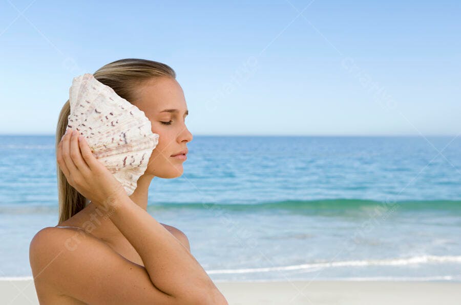 Mulher na praia ouvindo o mar concha