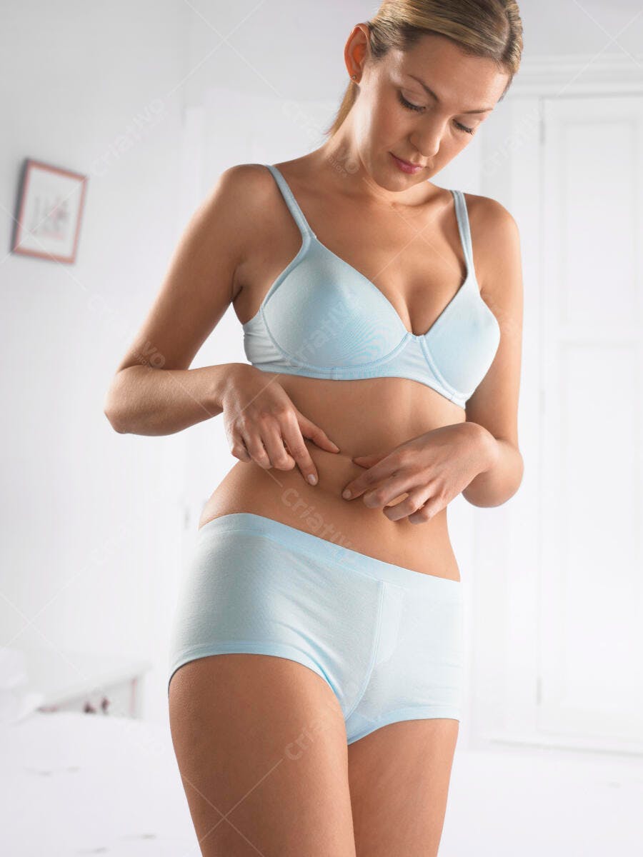 Mulher checando gordura abdominal em lingerie azul