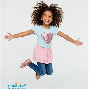Photo of a joyful Black girl with curly hair jumping. She's wearing a light blue t-shirt with a sparkly pink heart, pink skirt and jeans. The image has a white background and conveys a feeling of joy and innocence.