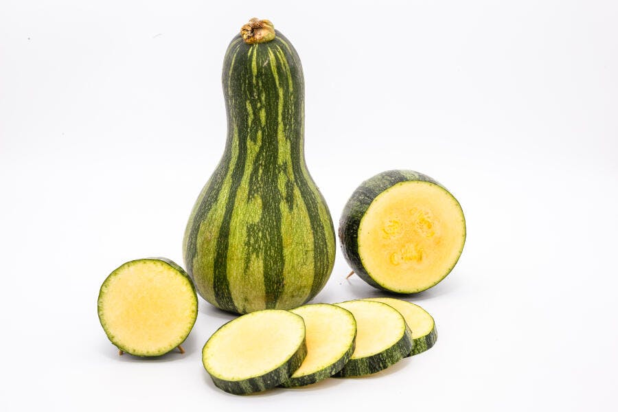 Abobrinha verde listrada inteira e fatiada em fundo branco puro