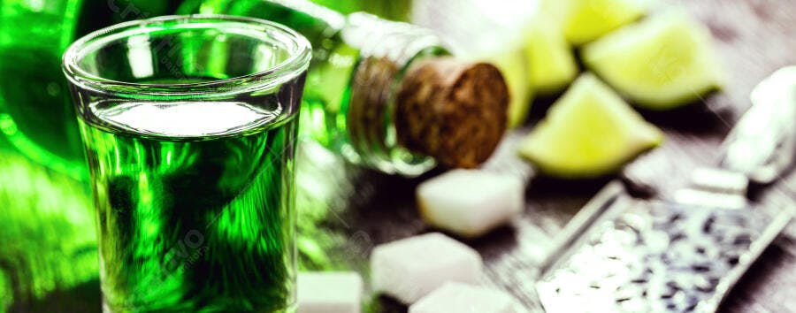 Shot de absinto verde brilhante com limão e açúcar em mesa escura