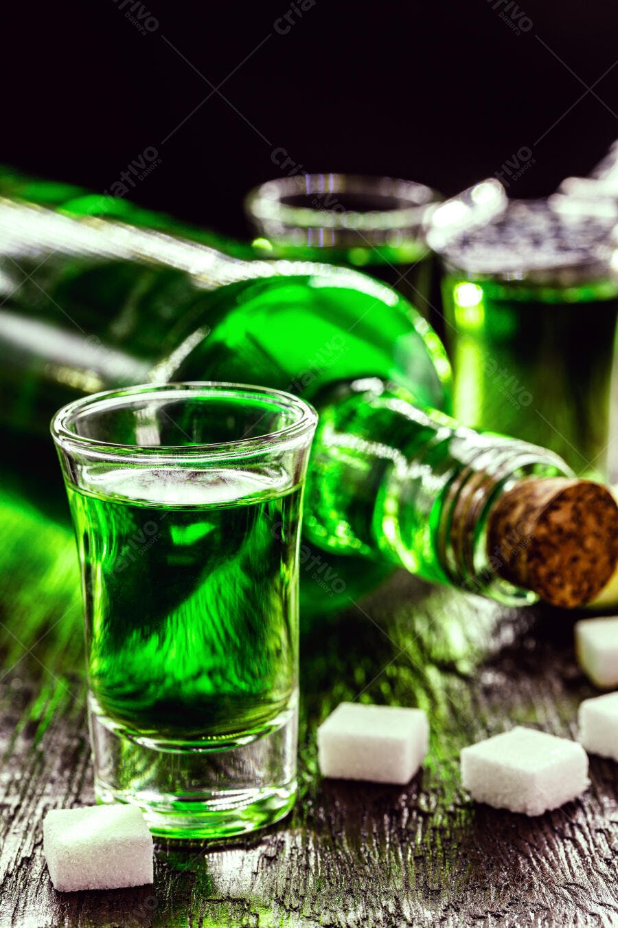 Absinto verde vibrante em copo de shot com garrafa e açúcar na mesa escura