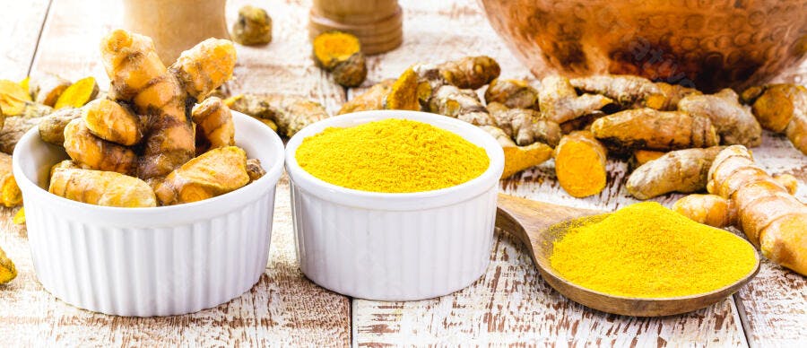Cúrcuma raízes frescas e pó amarelo vibrante em tigelas brancas na madeira