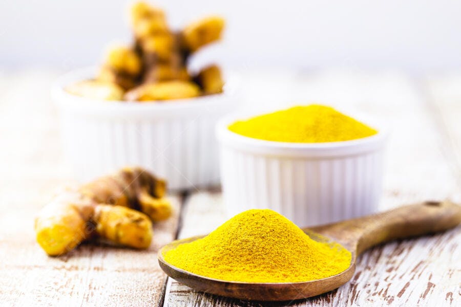 Cúrcuma em pó amarela e raiz fresca em colher de madeira sobre mesa rústica
