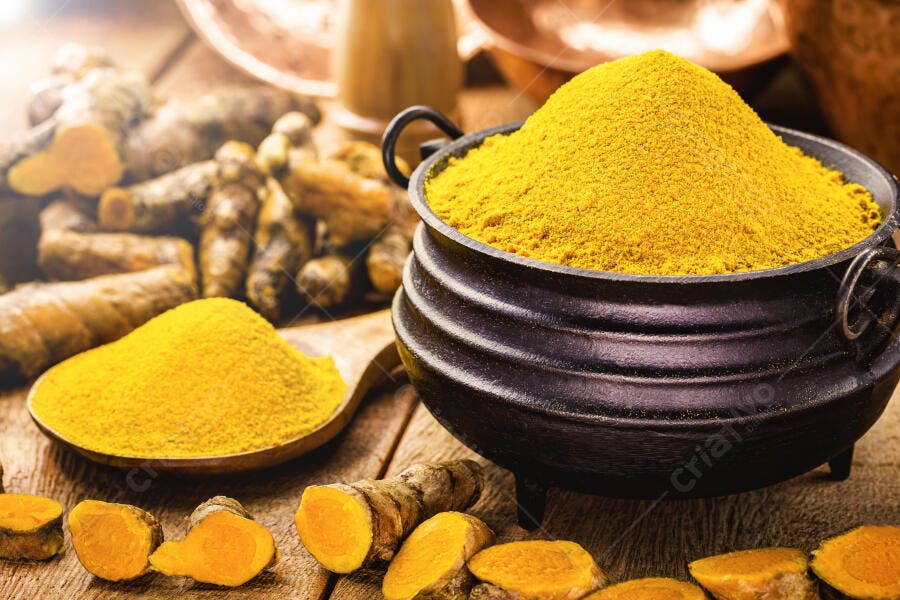 Cúrcuma em pó amarelo vibrante e raízes frescas em caldeirão de ferro rústico