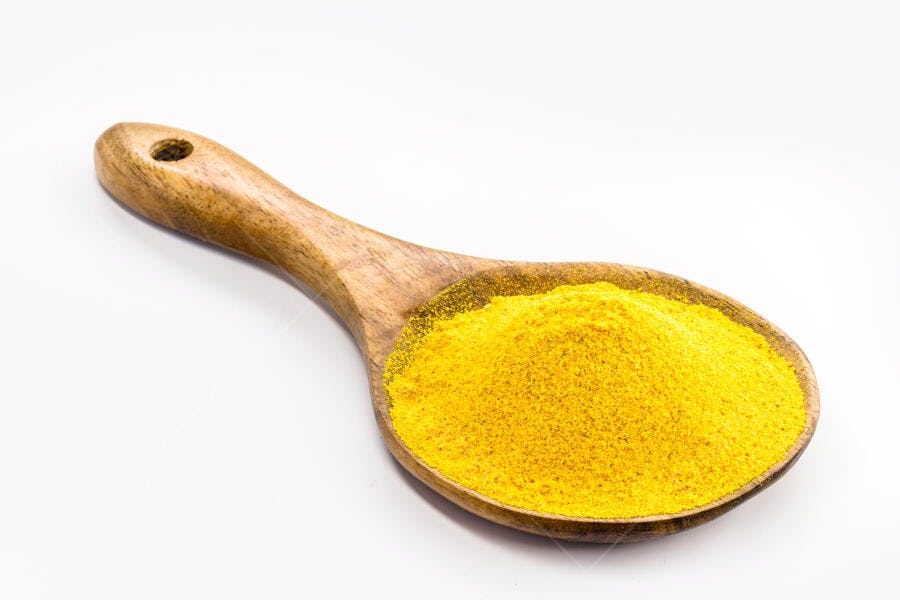 Colher de pau com pó amarelo vibrante em fundo branco