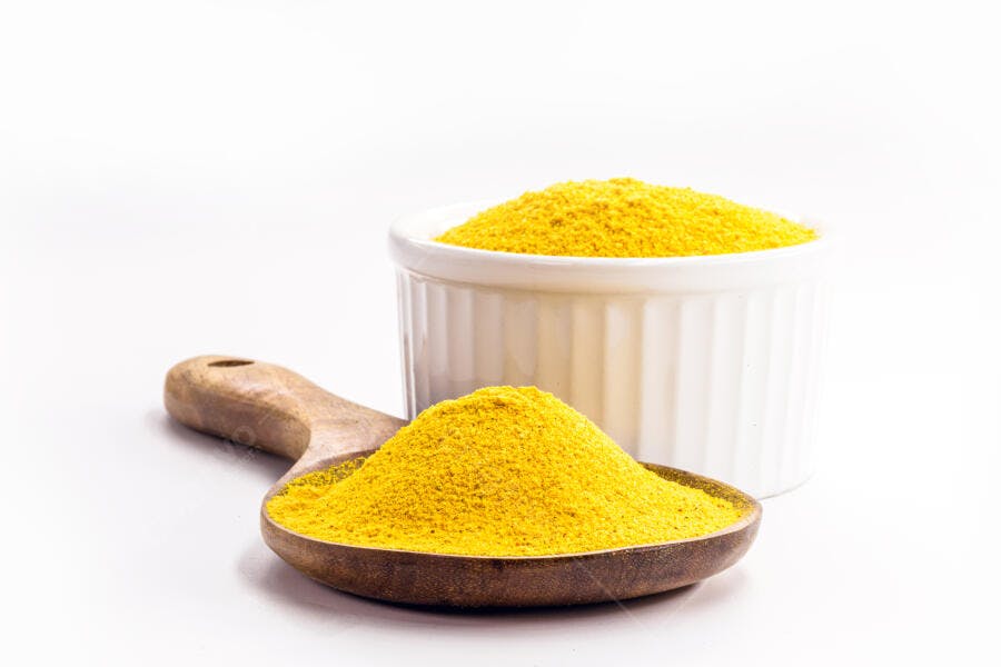 Pó amarelo brilhante em colher de madeira e tigela branca