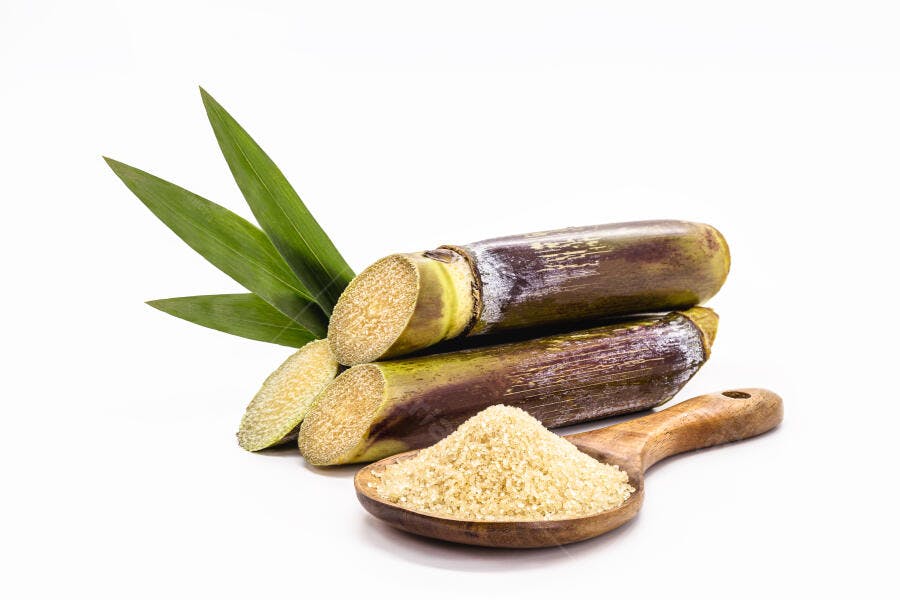 Cana-de-açúcar e açúcar mascavo granulado em colher de pau fundo branco