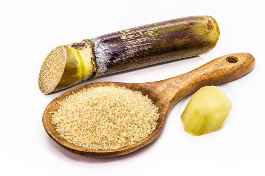 Cana-de-açúcar e açúcar mascavo em colher de madeira sobre fundo branco