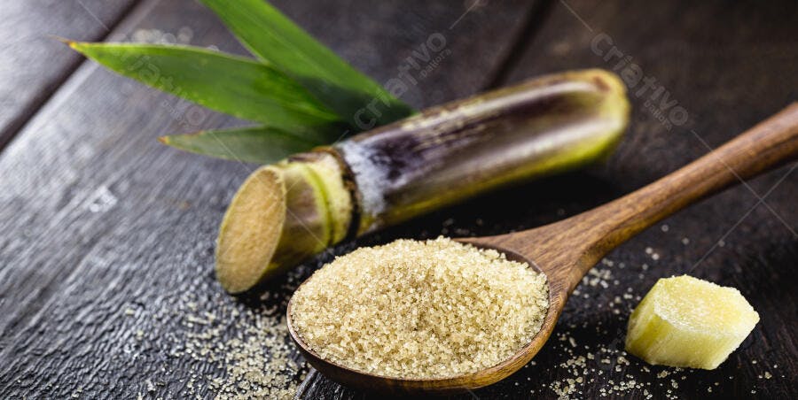 Cana-de-açúcar e açúcar mascavo em colher de pau sobre madeira escura