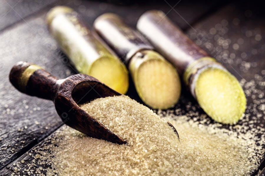 Açúcar mascavo em colher de madeira e pedaços de cana em mesa escura