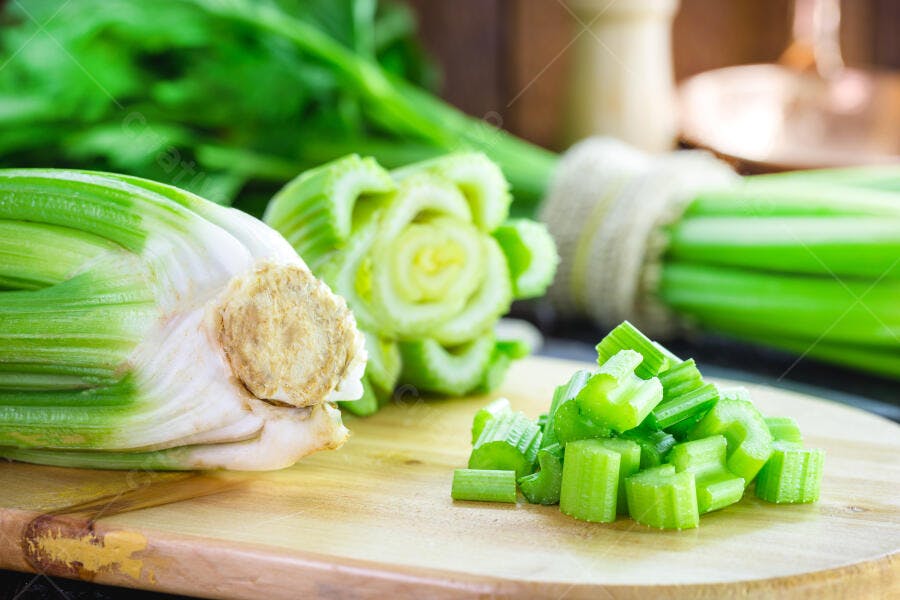 Aipo fresco picado e inteiro sobre tábua de madeira na cozinha