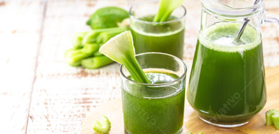 Suco verde de aipo e limão em copos e jarra sobre mesa de madeira clara