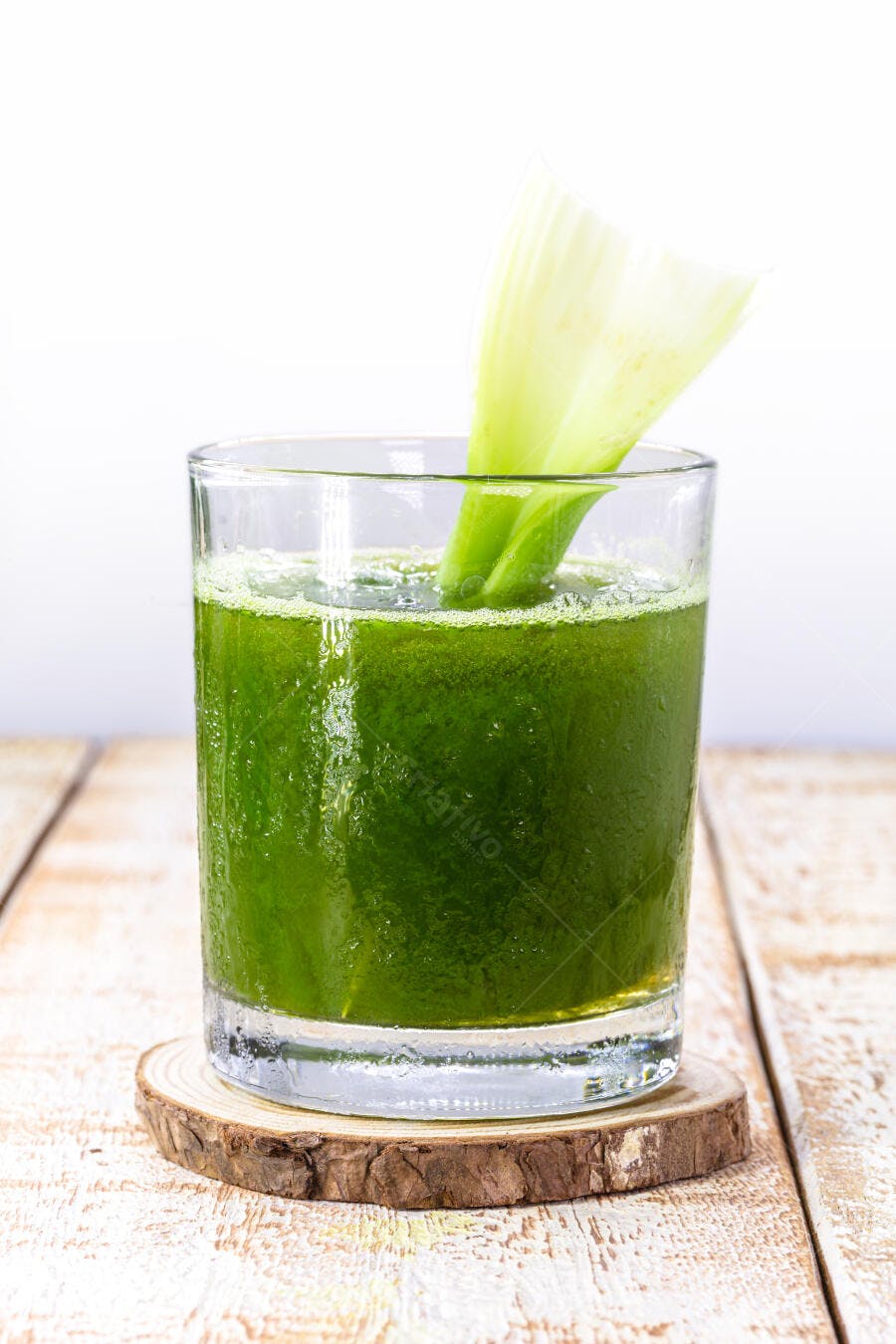Suco verde com talo de aipo em copo gelado sobre madeira clara