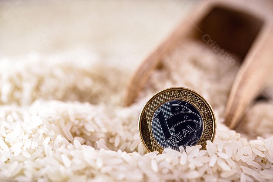 Moeda de um Real dourada e prateada sobre arroz branco cru com colher de madeira clara