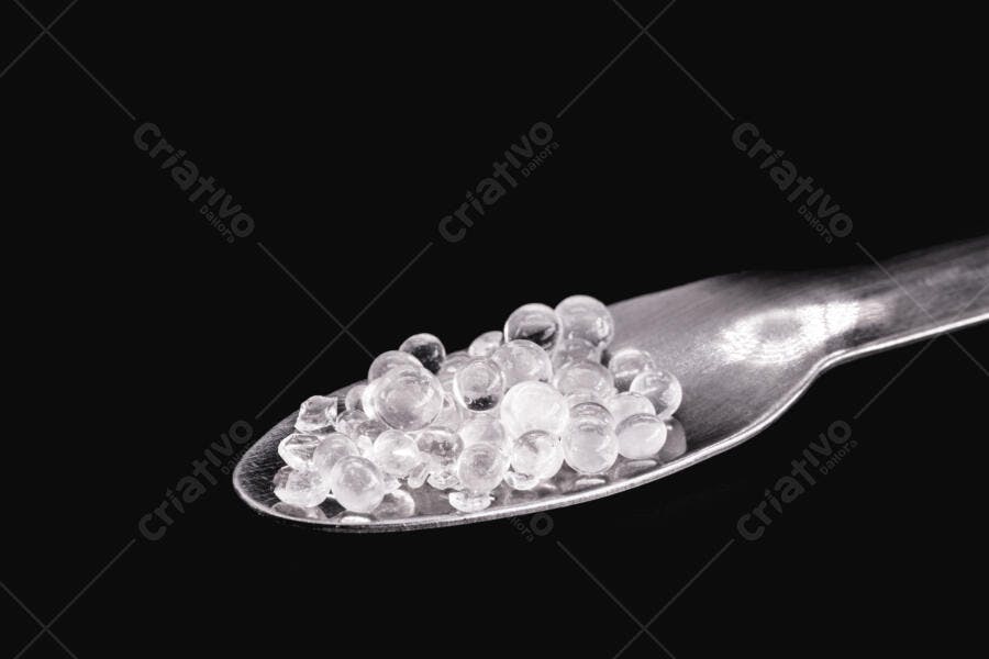 Grânulos transparentes em colher de metal sobre fundo escuro