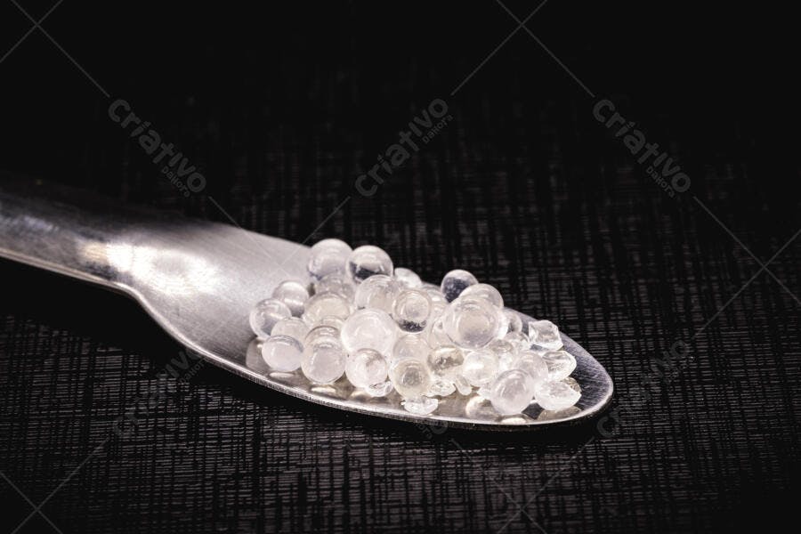 Esferas de sílica gel transparentes em colher de metal sobre fundo preto