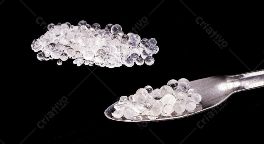 Esferas de sílica gel transparentes com colher metálica em fundo preto de estúdio