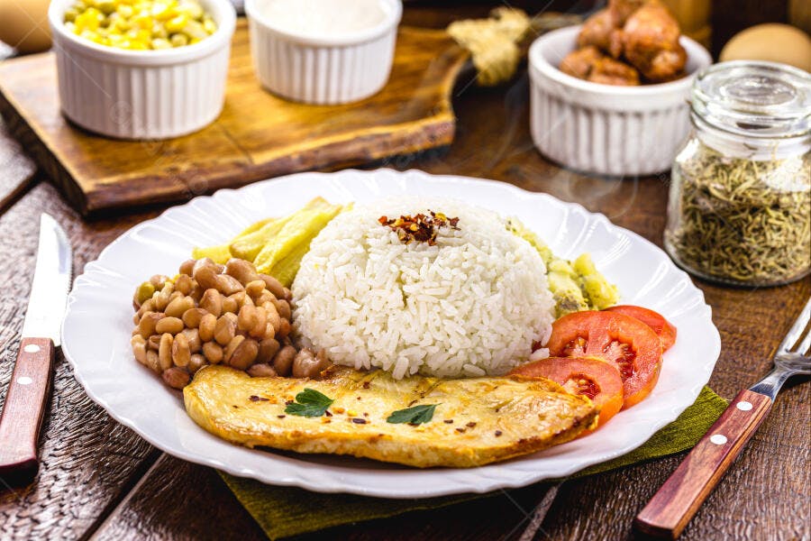Prato de peixe grelhado com arroz feijão batata frita e tomate em mesa rústica