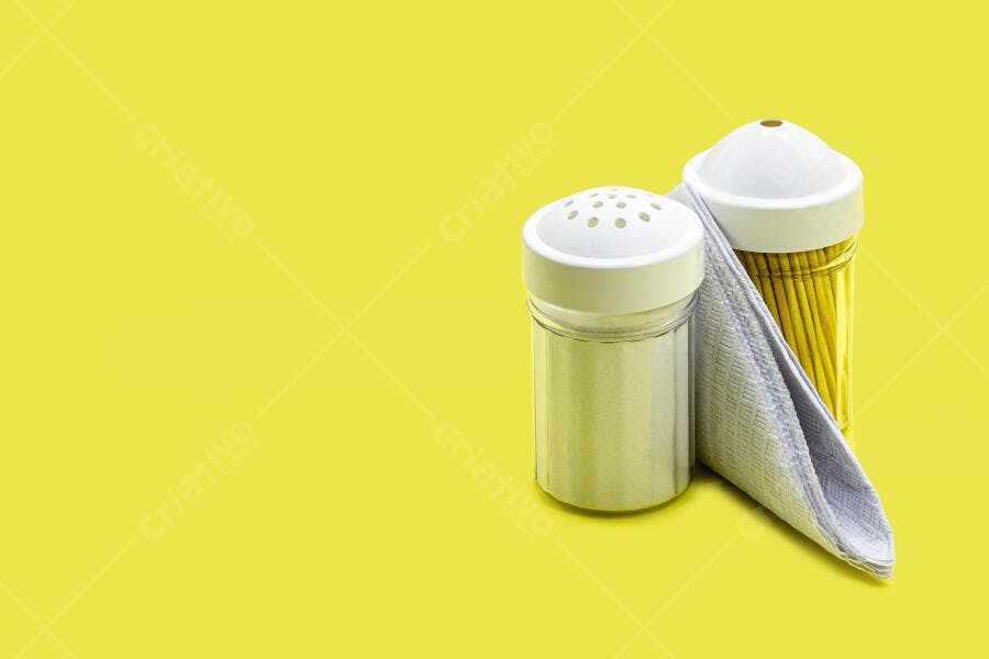 Saleiro e paliteiro brancos com guardanapo em fundo amarelo vibrante