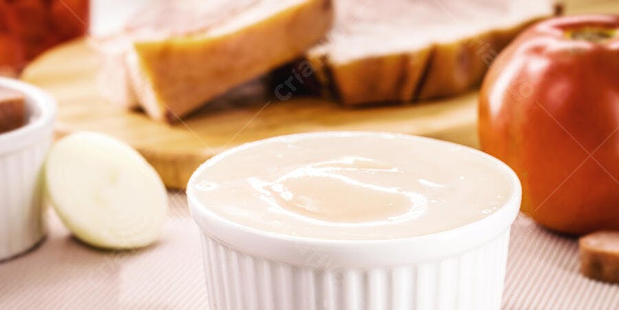 Molho branco cremoso em ramekin cercado por carne assada tomate e cebola