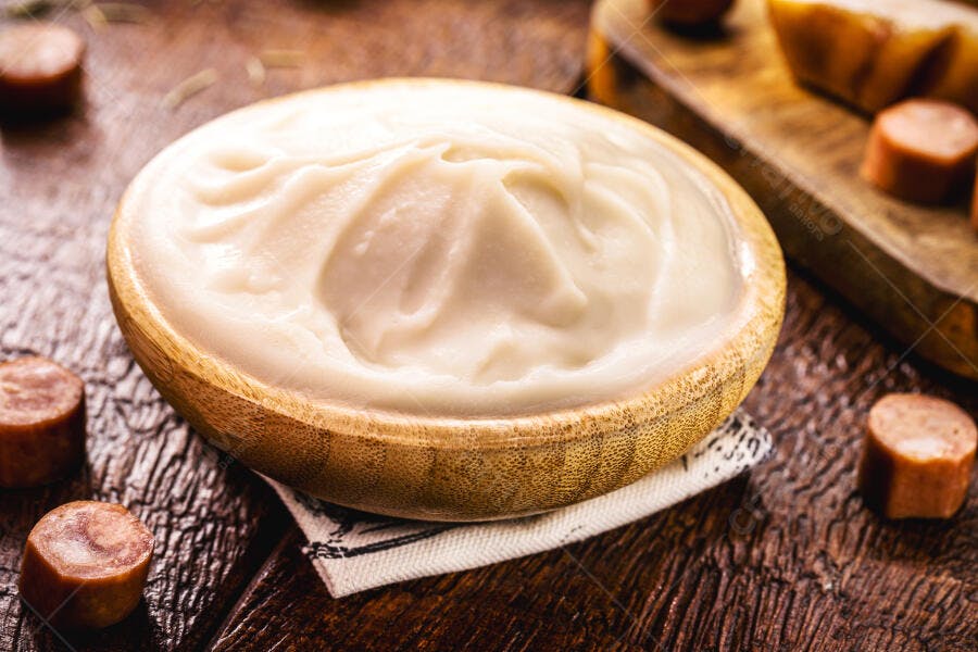 Creme branco em tigela de madeira com linguiça fatiada e tábua rústica