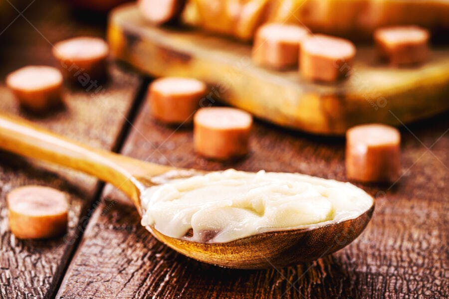 Colher de madeira com maionese cremosa e salsichas fatiadas em mesa rústica
