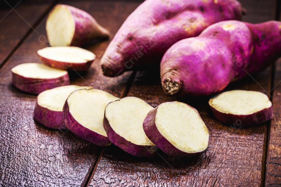 Batata doce roxa inteira e fatiada em mesa de madeira rústica