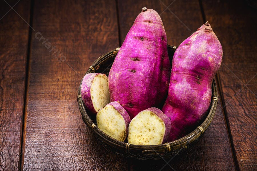 Batatas doces roxas em cesto rústico sobre mesa de madeira algumas fatiadas frescas