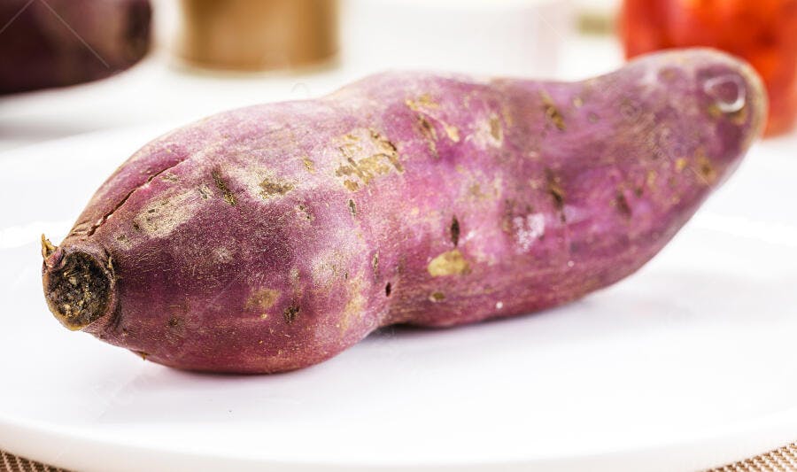 Batata doce roxa crua fresca em prato branco com resíduos de terra