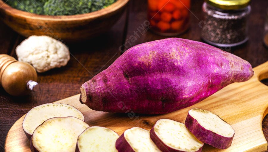 Batata doce roxa cortada em tábua de madeira com vegetais frescos
