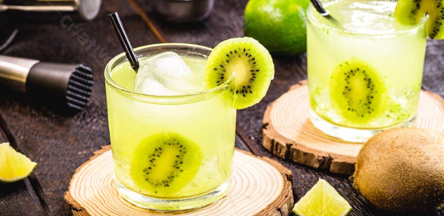 Caipirinha de kiwi verde com gelo e rodelas de lima em mesa de madeira