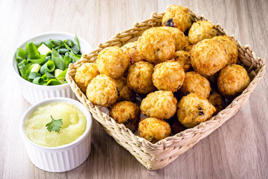 Bolinhos fritos dourados em cesta rústica com molho e cebolinha fresca