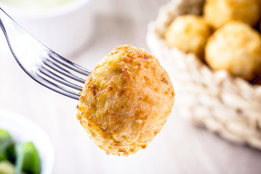 Bolinho frito crocante no garfo com cesto ao fundo comida brasileira