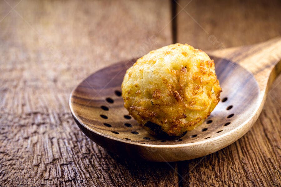 Bolinho frito dourado em colher de pau rústica sobre mesa de madeira