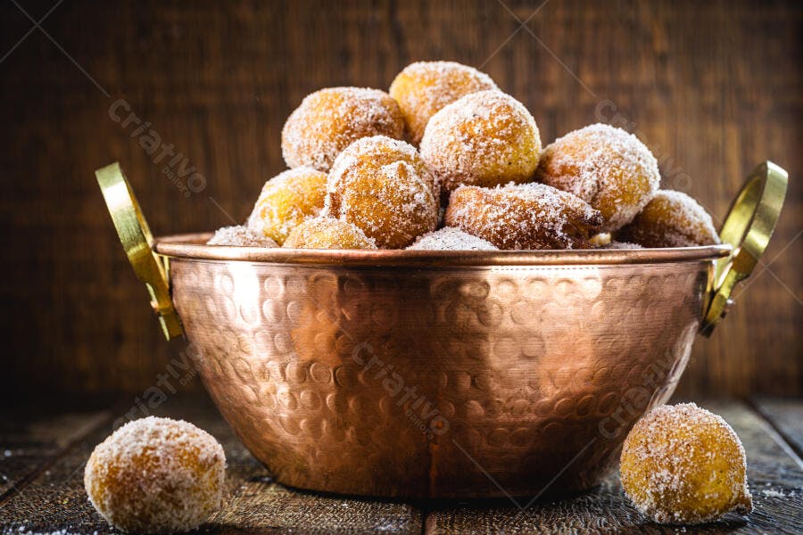 Bolinhos de chuva dourados em tigela de cobre sobre mesa de madeira rústica