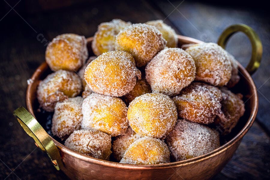 Bolinhos de chuva dourados em tigela de cobre com açúcar granulado