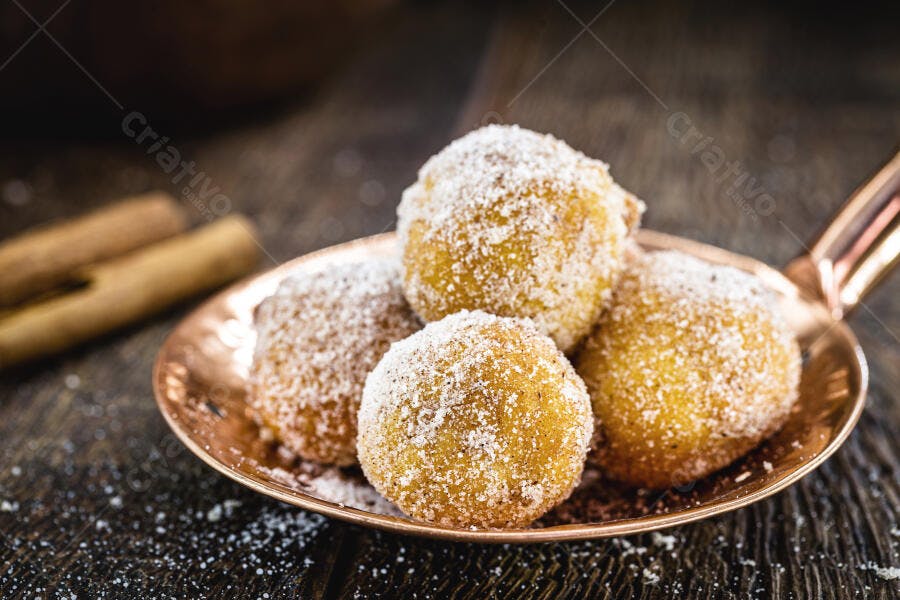 Bolinhos de chuva dourados com açúcar e canela em prato cobreado
