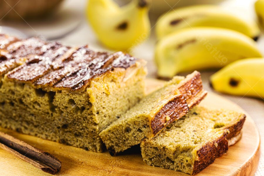 Pão de banana fatiado em tábua de madeira com canela e frutas frescas