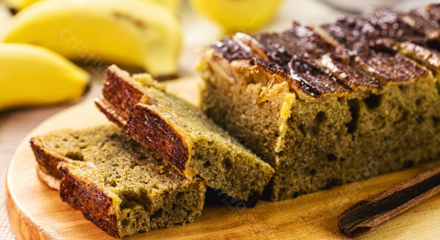 Bolo de banana fatiado em tábua de madeira com frutas frescas no fundo