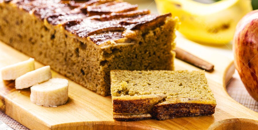Pão de banana fatiado em tábua de madeira com frutas e canela