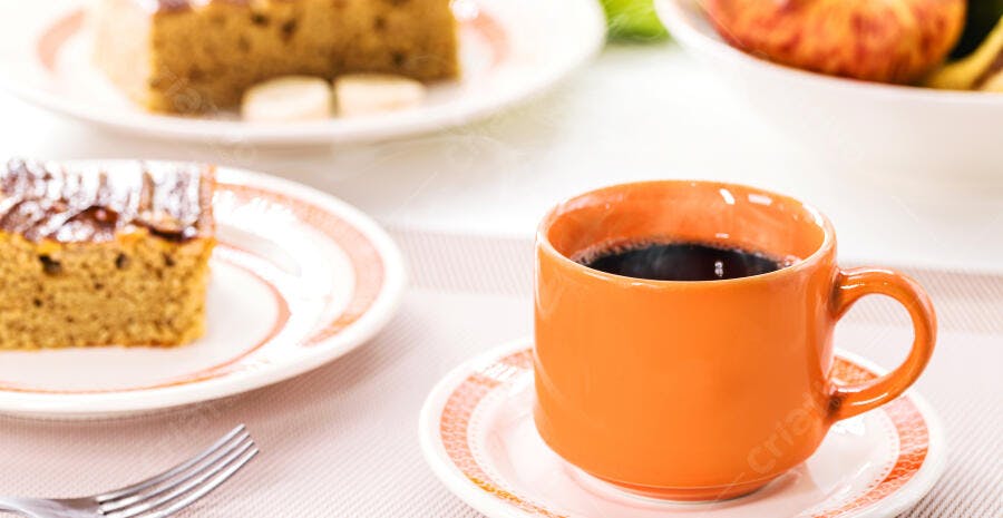 Caneca laranja de café quente com bolo de café da manhã na mesa