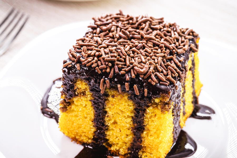 Fatia de bolo de cenoura com cobertura de chocolate e granulado em prato branco