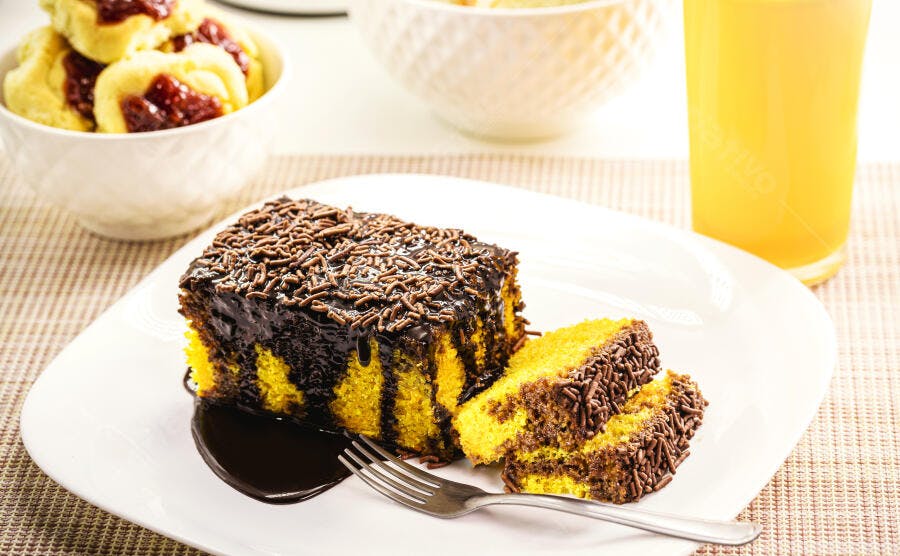 Bolo de cenoura amarelo com cobertura de chocolate granulado e suco de laranja