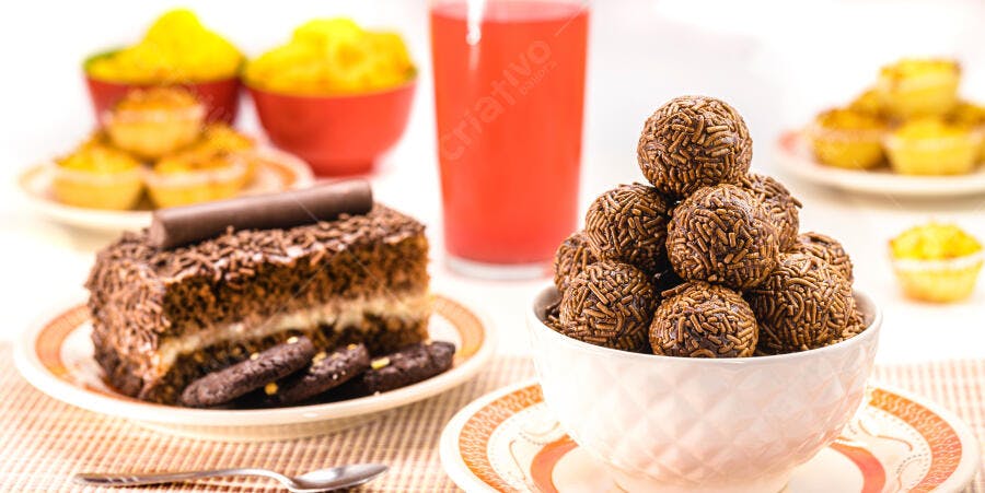 Brigadeiros e bolo de chocolate com granulado em mesa festiva com suco vermelho