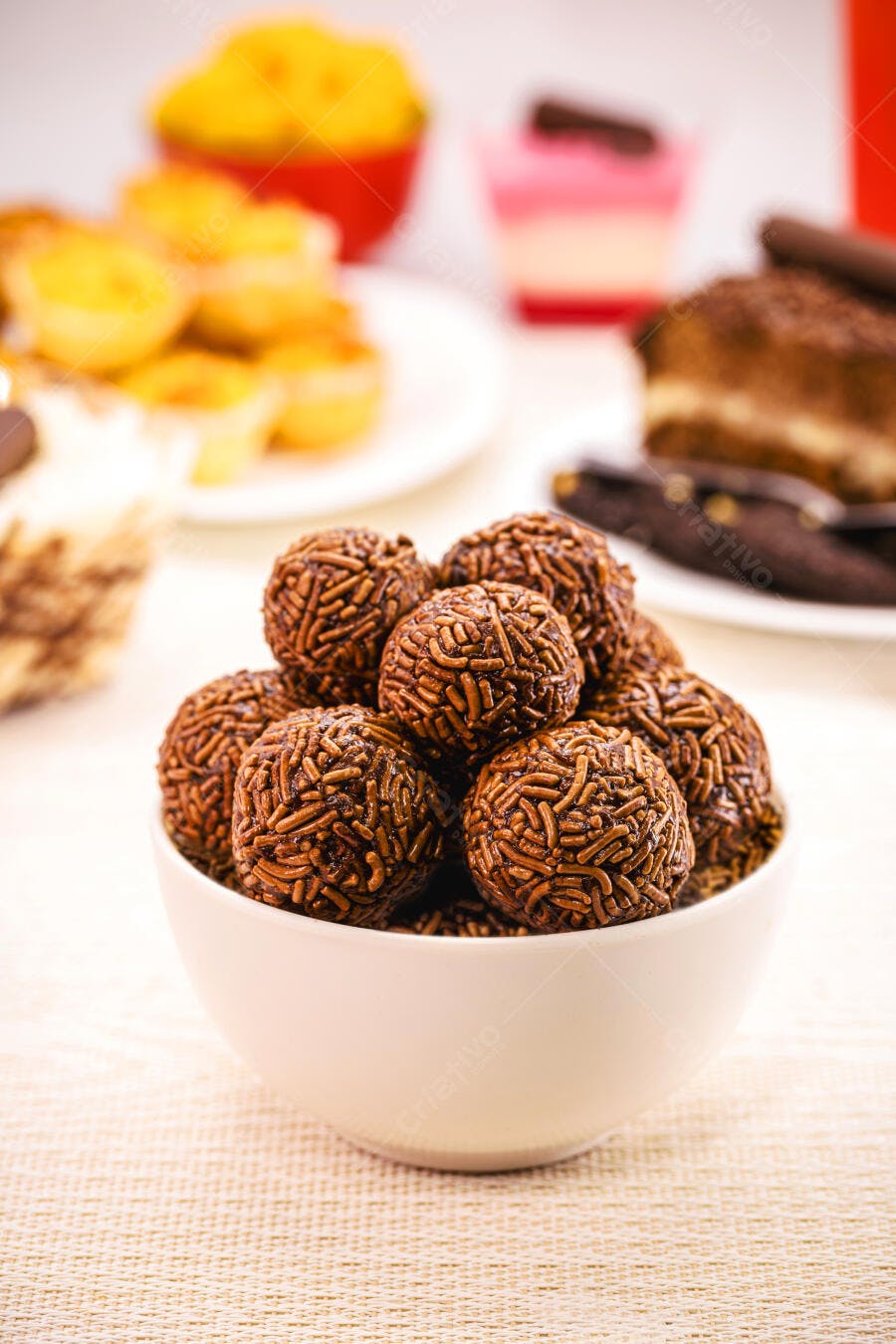 Brigadeiros de chocolate ao leite em tigela branca com doces de festa