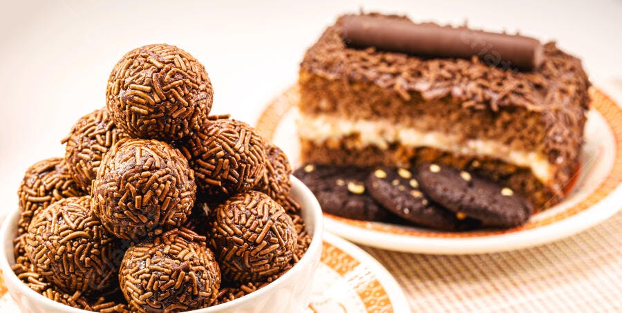 Brigadeiros de chocolate em tigela com bolo e biscoitos ao fundo