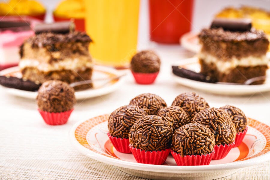 Brigadeiros de chocolate em forminhas vermelhas sobre mesa com bolo de festa